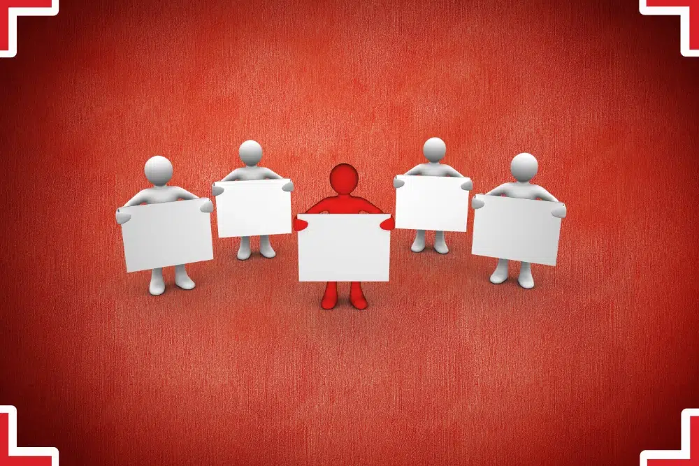 Illustration of a red figure standing among four white figures holding blank placards, representing a red team review of a federal proposal Illustration of a red figure standing among four white figures holding blank placards, representing a red team review of a federal proposal